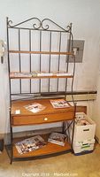 Full view of metal and wood bakers rack with several magazines on shelves and on floor nearby