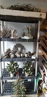 Full view of Rubbermaid shelf with Christmas decorations on all shelves, including silver pine cones, wreath, ball ornaments, decorative houses and tabletop trees.