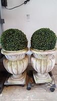 Two large plastic planters with green artificial shrub balls inside, showing overall wear and scratches.