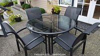 Full set of round glass-top table and four mesh sling chairs on patio