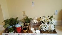 Photo showing various metallic, ceramic, and glass vases arranged with artificial foliage and flower bunches along with decorative shells.