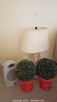 Full view showing table lamp, two artificial green potted plants in red pots, and the Lasko electric heater on carpet.