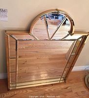 Full view of rectangular metal framed mirror with arched top section and geometric paneling, lying against wall on hardwood floor.