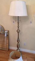 Full view of the 69 inch tall metal floor lamp in a brass-like finish with a white lampshade on top.