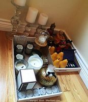 Overall lot overview showing glass candle holders with white candles, Buddha figurines, pear candles, and Laduree Matryoshka set in boxes