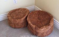Two round, soft leather Moroccan foot stools with detailed embossed patterns placed on carpet against wall.
