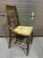 Side view of the antique wooden chair showing the wooden frame, turned legs, and worn tapestry seat.