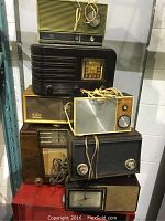 Overall view showing stacked 7 antique radios of varying sizes and finishes including wood and Bakelite.