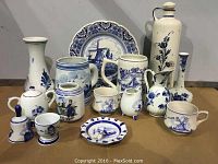 Full view of all 15 hand painted Delft pottery items arranged on table showing various vases, plates, cups, and decorative pieces with blue and white colors and Dutch designs.