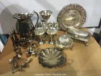 Full view of all silverplate items including trays, butter dishes, goblets, shakers, utensils, jug, cup, napkin ring, and egg cup arranged on table