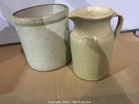 Photo displaying two stoneware pottery crocks of differing sizes on a flat surface under soft lighting.