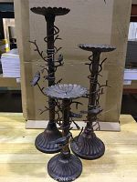 Three heavy metal candle holders grouped together showing varying heights and detailed branch and bird decoration wrapped around the stems.