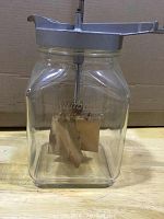 Front and side view of clear glass jar with embossed Sunbeam logo and wooden churn paddles inside.