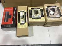 Four outdoor light fixtures in original boxes arranged on a white table, showing different styles and packaging.