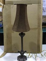 Full view of the lamp showing the brown tapered fabric shade and lamp base against a cardboard background.