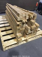 Photo of stacked assorted unfinished wooden railing balusters made of oak and maple on a wooden pallet showing different shapes and profiles.