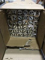 Open cardboard box containing 36 fluorescent tubes individually wrapped in cardboard sleeves, organized in a 6x6 grid.