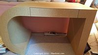 Front view of the woven grass cloth desk showing one drawer and curved side panel.