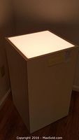Full view of illuminated pedestal cube showing lit top panel and smooth sides.