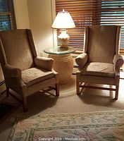 Two wing chairs in room with small round glass-top table and lamp