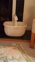 White ceramic basket placed near a fireplace on a hearth, showing basket front and handle detail, showcasing the woven wicker effect in ceramic