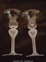 Pair of Lalique cordial glasses with frosted heart-shaped stems placed on black background.