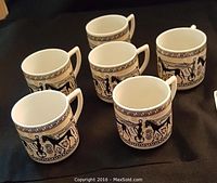 Set of six espresso cups displayed on a black surface showing the detailed black-figure Greek designs and angular handles.