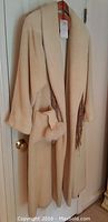 Full view of cream shearling alpaca coat hanging on door with matching gloves and gold scarf visible.