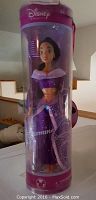 Photo of one of the Disney Princess Jasmine dolls in original clear cylindrical packaging, showing purple outfit and doll face details.