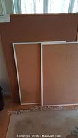 Three cork boards propped up against a wall, two smaller boards with white frames and one larger unframed board behind them.
