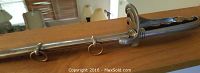 Ornamental sword with metal sheath resting on a wooden surface, showing the curved handle and rings on the sheath.