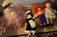 Raggedy Ann, Raggedy Andy, Heritage Porcelain Doll, and Bride Doll on floor showing clothing and features