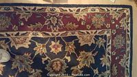Close-up of the rug showing navy center with floral motifs and dark red border with cream separating line.