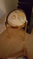 Full view of the vintage globe mounted on a brass stand showing the globe's size and stand style.