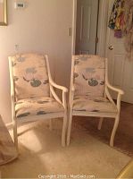 Two upholstered arm chairs with painted wood trim and crewel fabric upholstery, placed side by side in a room.