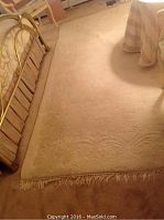 Full view of ivory hand woven sculptured rug on floor beside brass bed frame, showing overall condition and size.