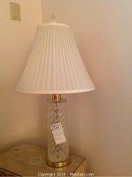 Full view of Waterford crystal table lamp including metal base and pleated light-colored fabric shade on a wooden table.
