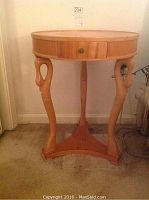 Front view of round wooden table with three carved legs and a drawer with knob.