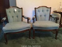 Full front view of two matching wood and upholstered parlor chairs with tufted backs, curved arms, and cabriole legs.