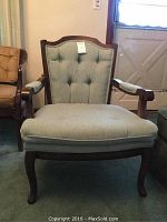 Front view of the wooden framed parlor chair with button-tufted upholstered backrest and cushioned seat in light grey fabric, showing normal wear.