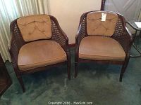 Pair of retro-style matching rattan chairs with gold upholstery on a carpeted floor.