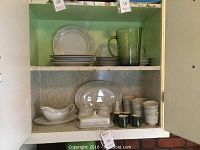 White china and green glassware in cabinet, showing plates, cups, saucers, gravy boat, cream and sugar, butter dish, salt shaker, serving platter, and green creamers and pitcher