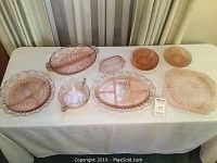 Full view of the eight piece pink depression glass lot arranged on a white tablecloth, showing variety of serving plates and bowls of different shapes and sizes.