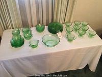 Lot overview of green Depression Glass set including plates, bowls, cups, saucers, sugar bowls, and serving bowl arranged on a table.