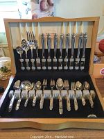 Full view of the flatware set neatly arranged inside the original wooden storage case with satin lined lid, showcasing knives, forks, spoons, serving spoons and resting slots.