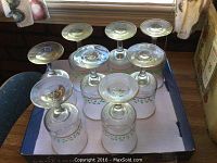 Top view of eight clear stemmed glasses arranged upside down in a box, showing gold rims and holly berry decorations.