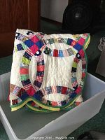 Folded view of the quilt showing colorful patchwork rings and yellow-green border, placed inside a translucent bin.
