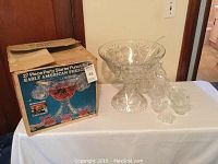 Full view of punch bowl set including box, punch bowl, ladle, and cups on a table