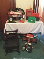 Photo of children's toys lot including Radio Flyer wagon with dolls, AMF Jr. tricycle, green plastic step, and wooden rocking chair in the foreground.
