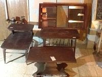Four wooden furniture pieces in basement: two-tier end table, coffee table, TV stand with plastic base, and wooden wall curio shelf with glass panels.